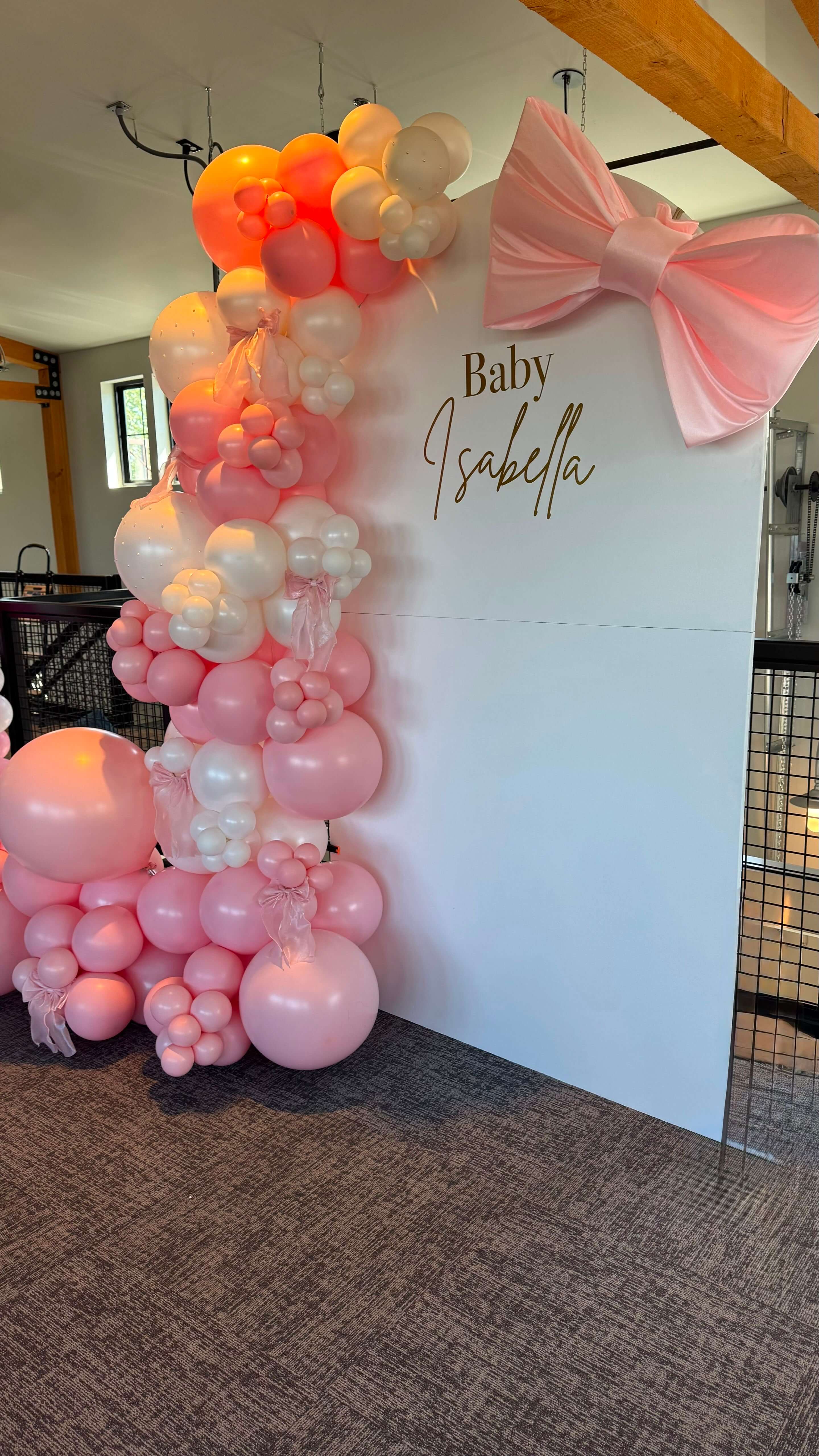 Blush pink and white balloon garland with a large satin bow on a 'Baby Isabella' backdrop for a baby shower
