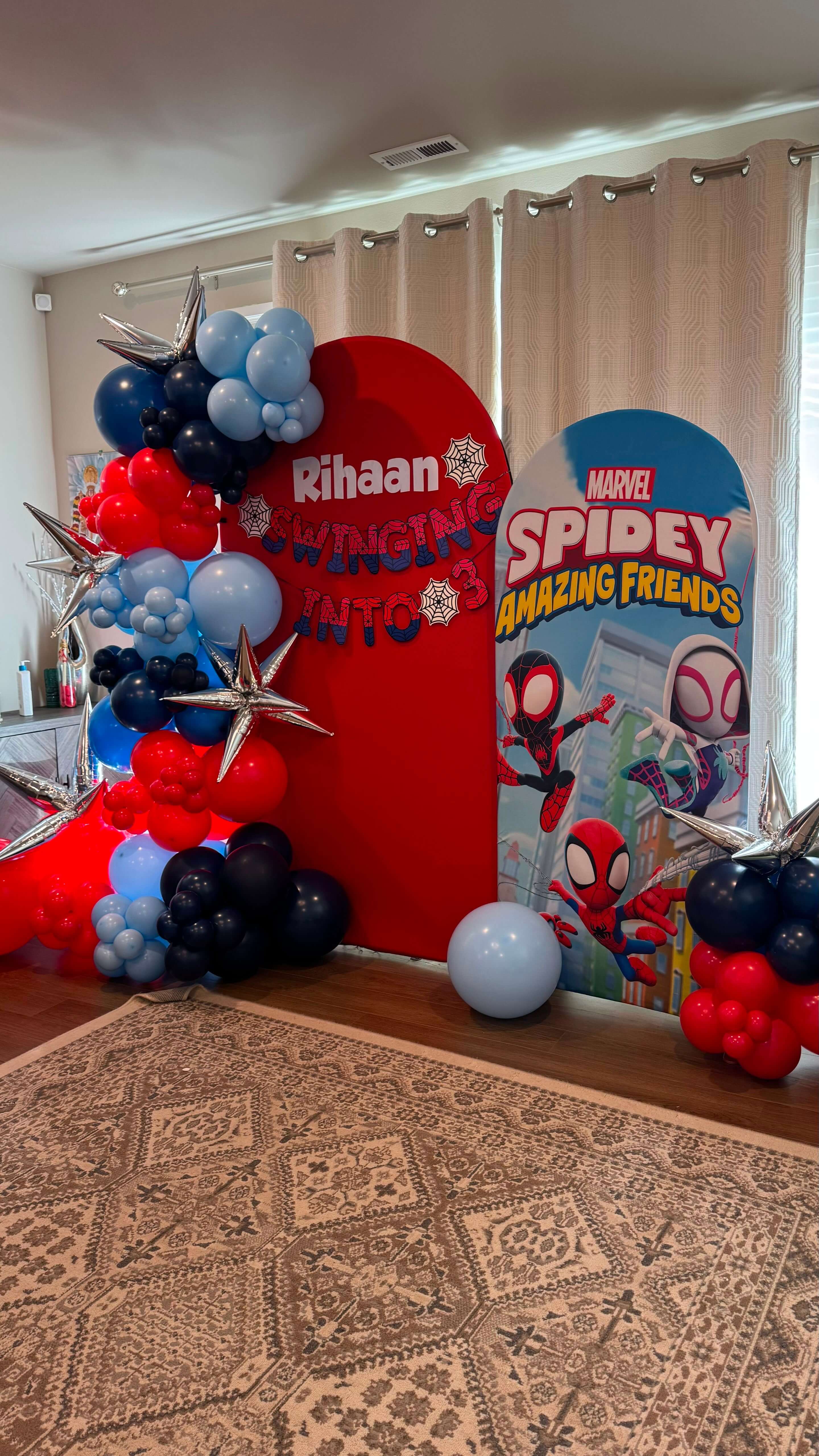 Spider-Man themed birthday setup with a red arch backdrop, red, blue and navy balloon garland and silver star foils for Rihaan's 3rd birthday